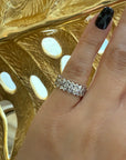 A hand with black nail polish wears Nijma M Fine Jewelry’s Marquise Diamond Eternity Ring, featuring marquise-shaped diamonds, set against a gold background with cut-out designs.