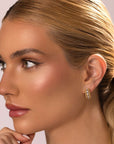 A woman with blonde hair in a sleek ponytail wears Nijma M Fine Jewelry's Small Diamond Hoop Earrings. Her smooth, glowing skin and natural makeup enhance her look as she gazes left against a light background.