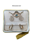 The Nijma M Fine Jewelry's Jewelry Pochette Case features a multi-purpose insert containing a necklace with an eye-shaped pendant, a pair of spiral earrings, and rectangular earrings. Its cushioned interior, adorned with yellow-gold braided edges and gold tassel detailing, keeps your precious jewels safe.