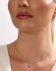 A woman with glossy lips and pulled-back hair is shown from the shoulders up, modeling the Nijma M Fine Jewelry Small White Gold Evil Eye Necklace and a small earring. She wears a white top.