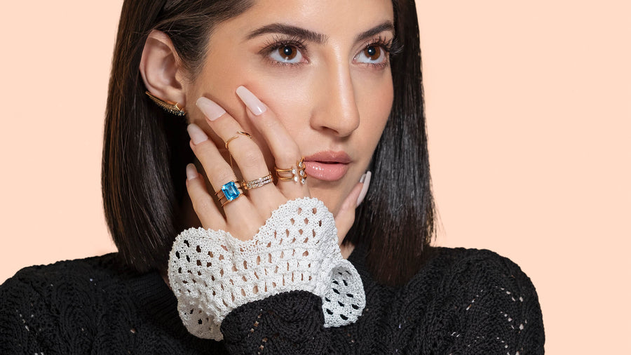 Woman modelling a variety of yellow gold rings - diamond, blue topaz, knuckle ring