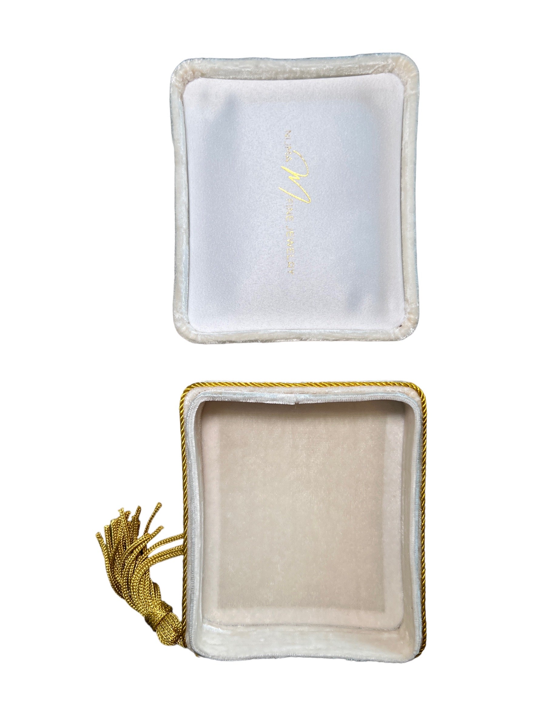 An open, empty Jewelry Pochette Case by Nijma M Fine Jewelry is presented as a white square box with elegant gold trim and intricate gold tassel detailing on one side. The detached lid is positioned above the box, showcasing a gold logo printed on the inside. The interior of this precious jewel safe is lined with soft white fabric.